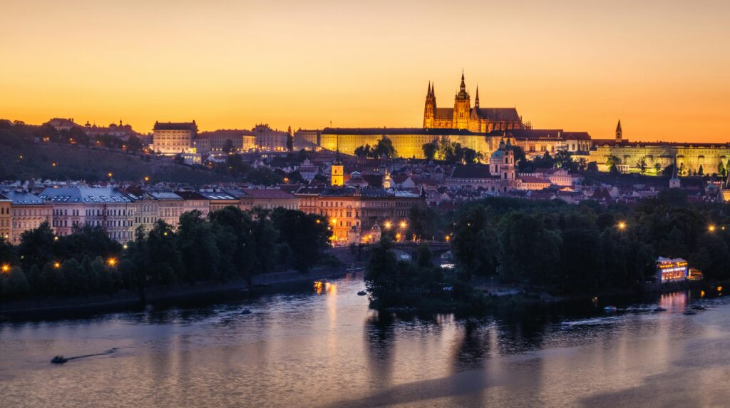 Scenic view of Prague Castle glowing at sunset with the Vltava River in the foreground.