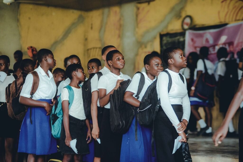 A group of schoolchildren in uniform lining up indoors, carrying backpacks.